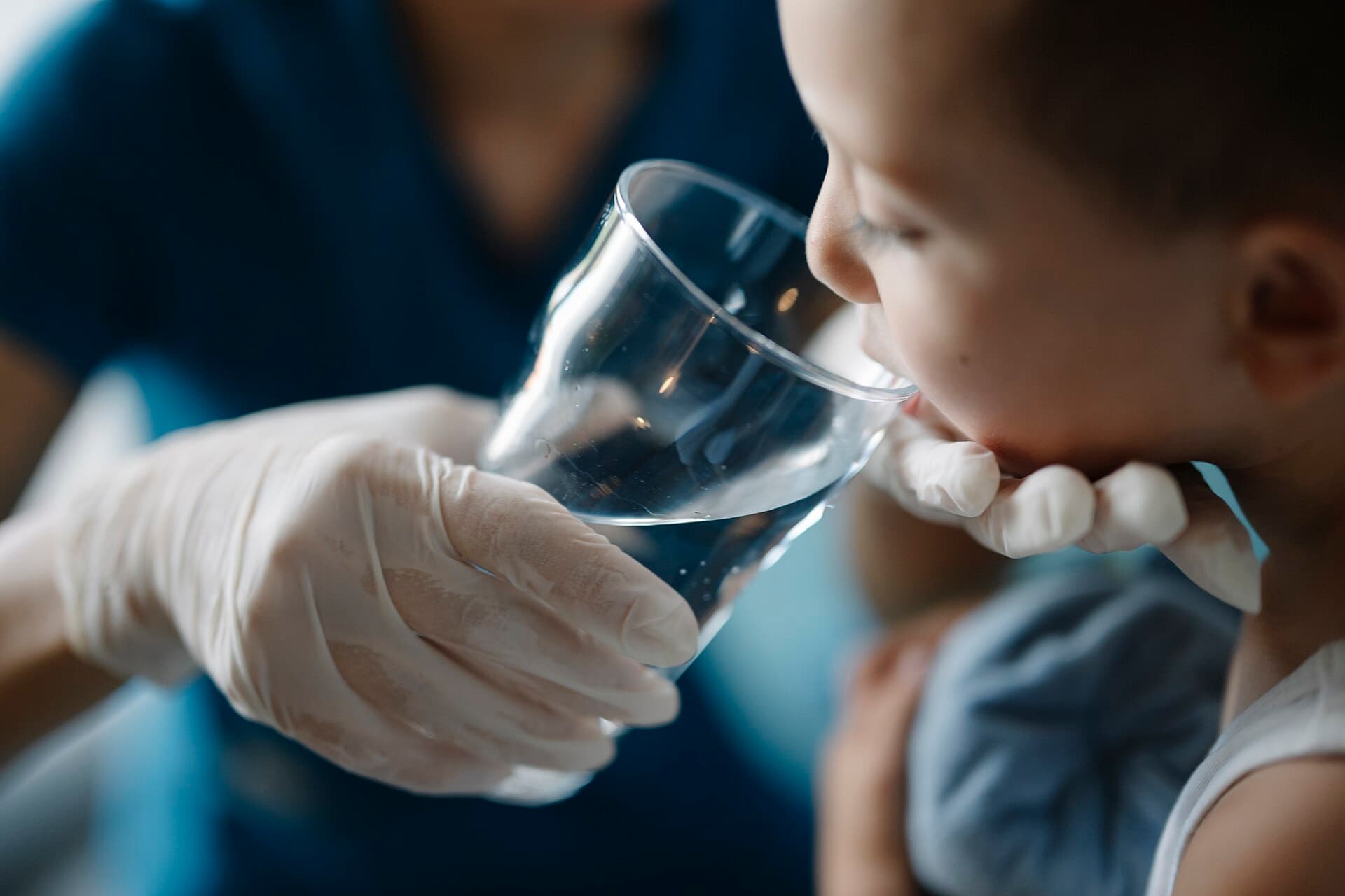 An adult holds a glass of water for a child to drink